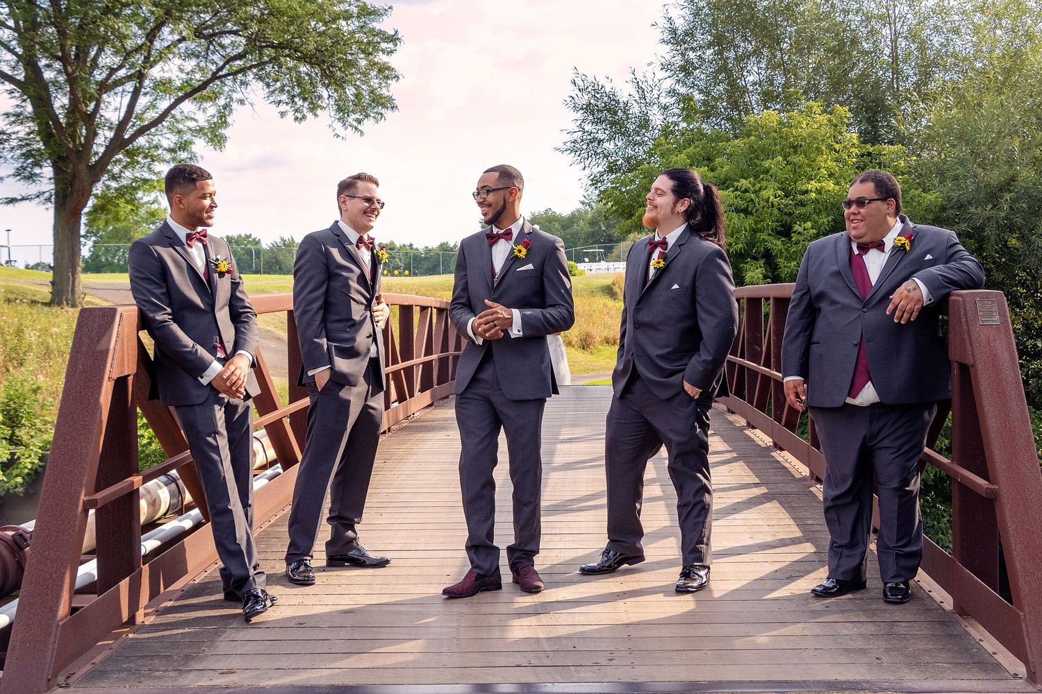 Groomsmen in navy suits gather on a wooden bridge for a casual group photo.