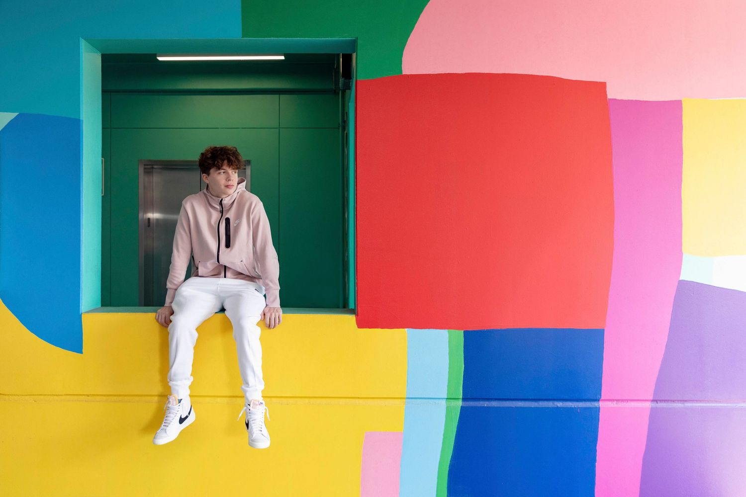 Artistic photo composition with person sitting against colorful geometric wall design.