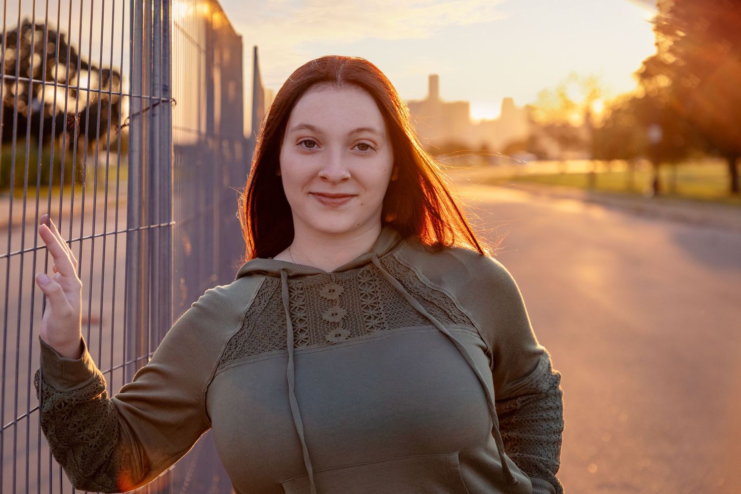 A sunset portrait by a fence featuring an olive green top with warm backlighting.