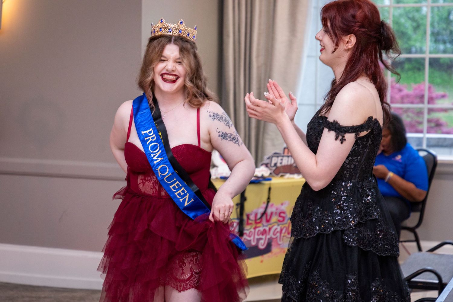 Group celebrating in formal attire with sashes and tiaras indoors.
