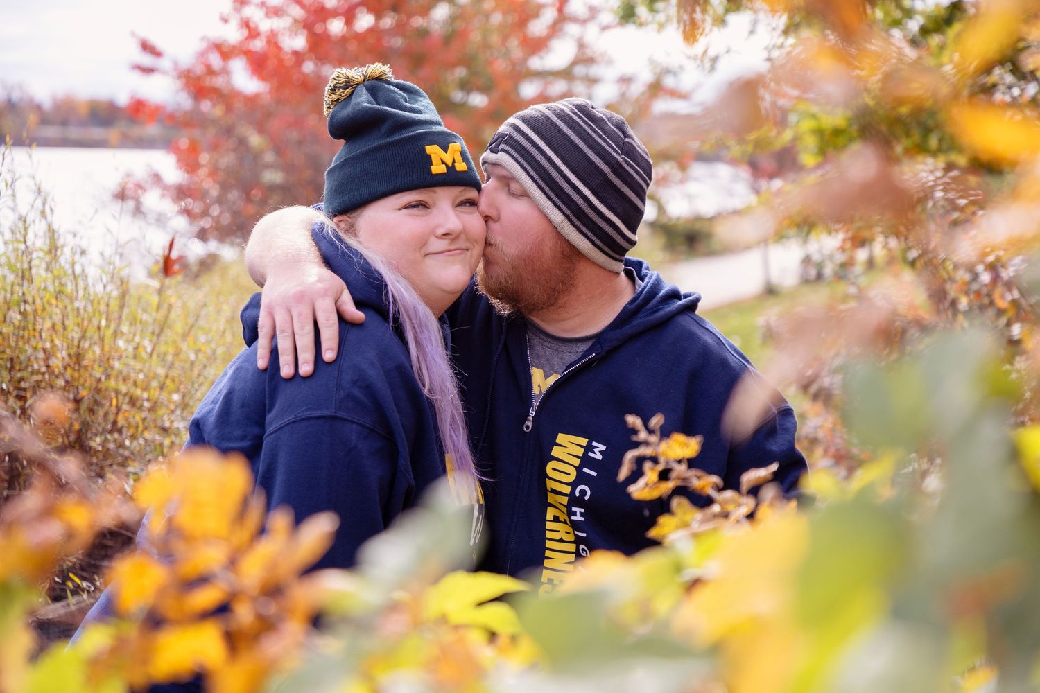 A couple shares an intimate moment among fall foliage wearing matching navy blue apparel.