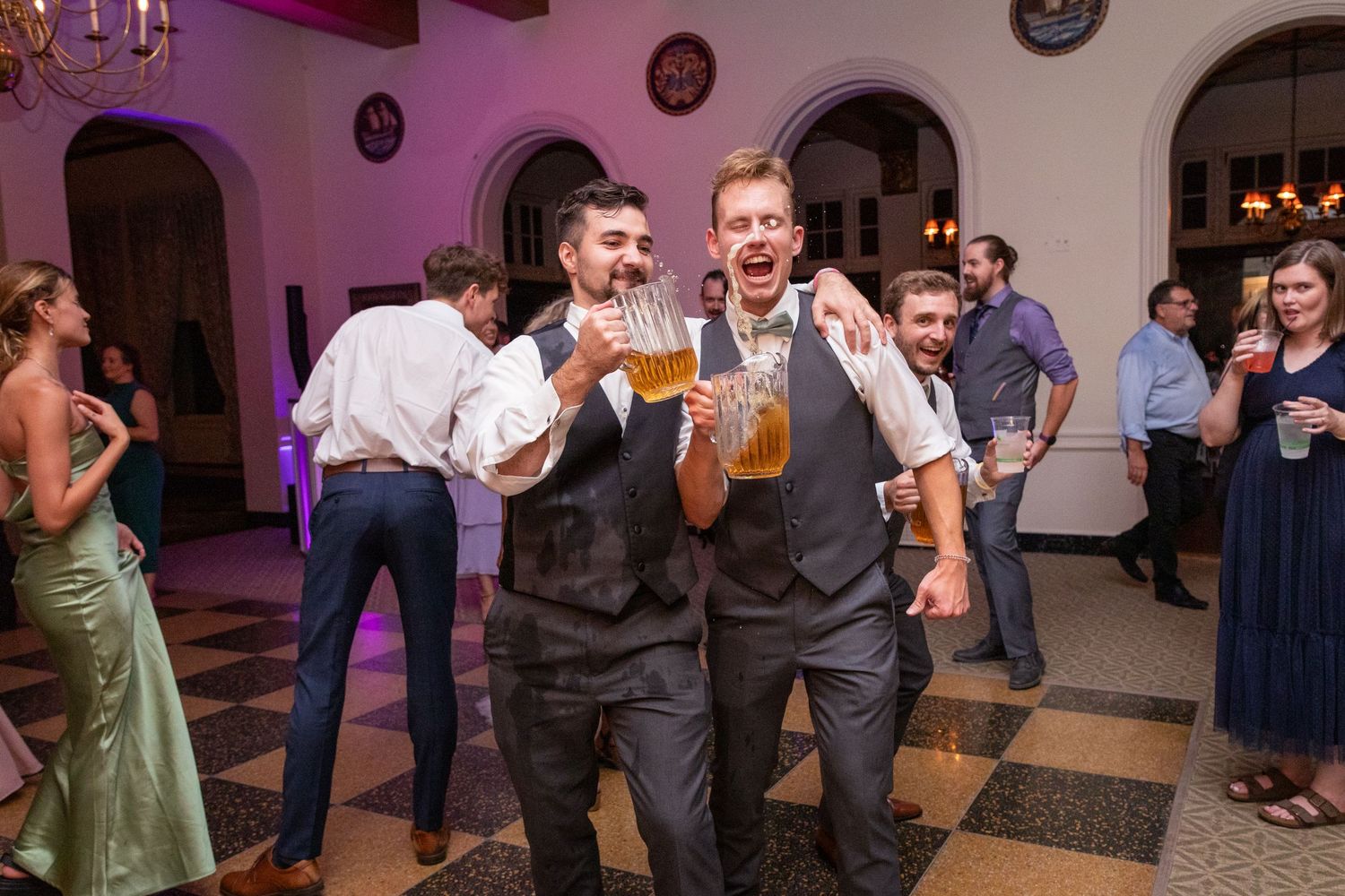 Wedding reception guests dancing and celebrating on a dance floor with purple lighting.