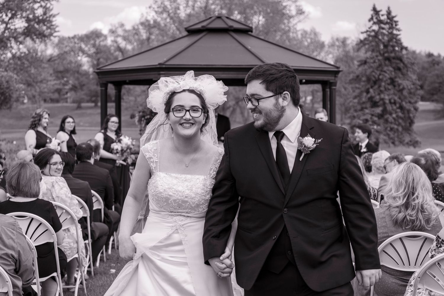 Outdoor wedding ceremony setup with black gazebo and white chairs on a cloudy day.