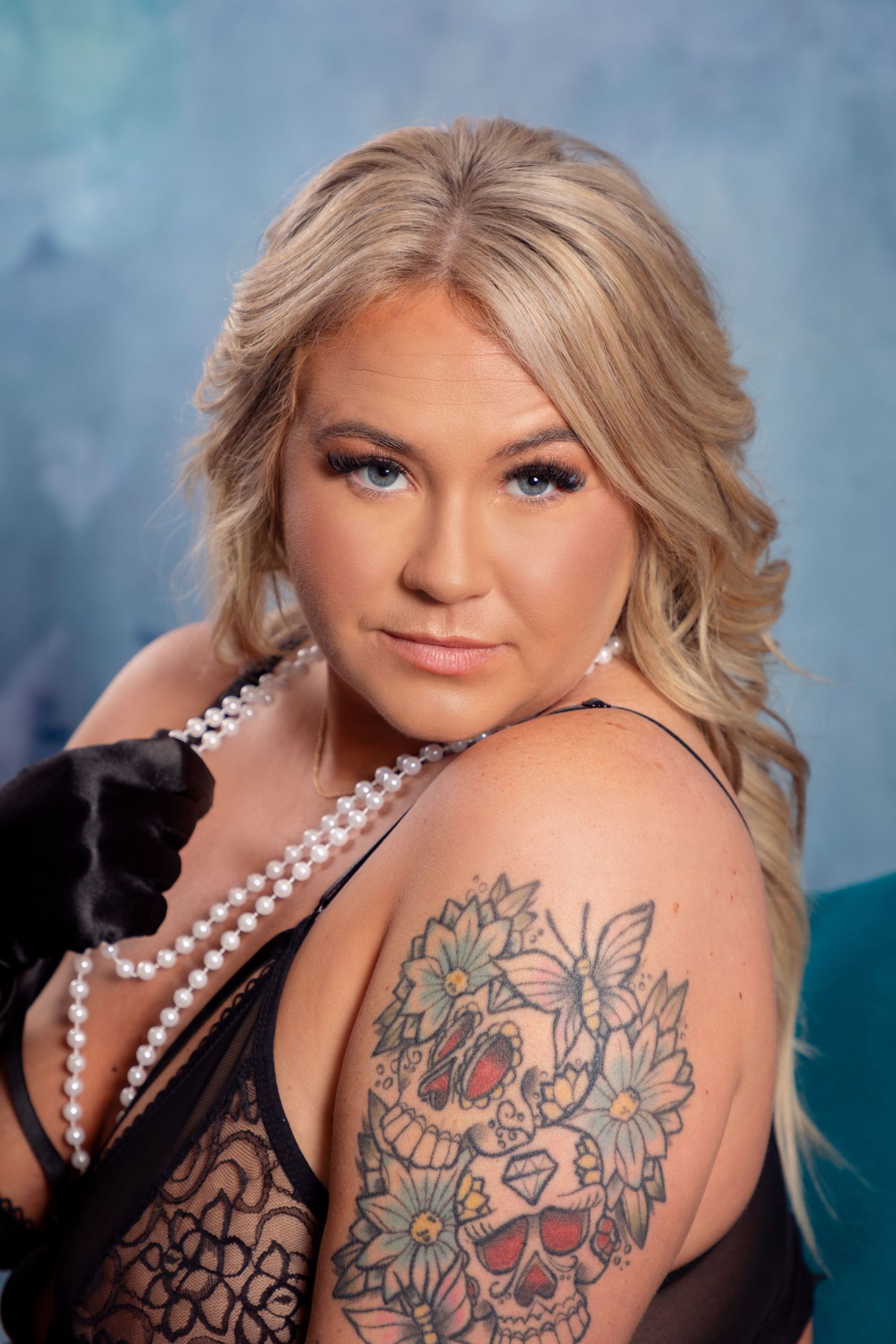Elegant boudoir portrait with pearl necklace, black gloves, and floral shoulder tattoo.