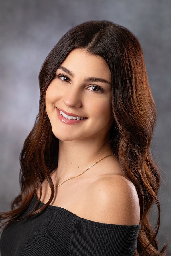 Professional studio portrait with off-shoulder black sweater against grey background.