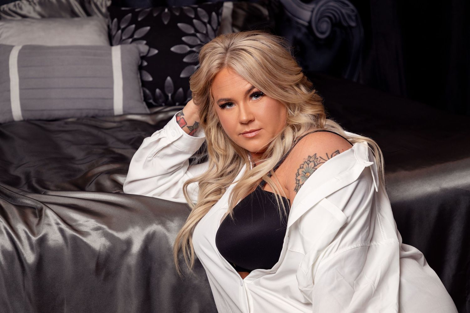 Glamour boudoir photo featuring black lingerie and white robe on grey satin bedding.