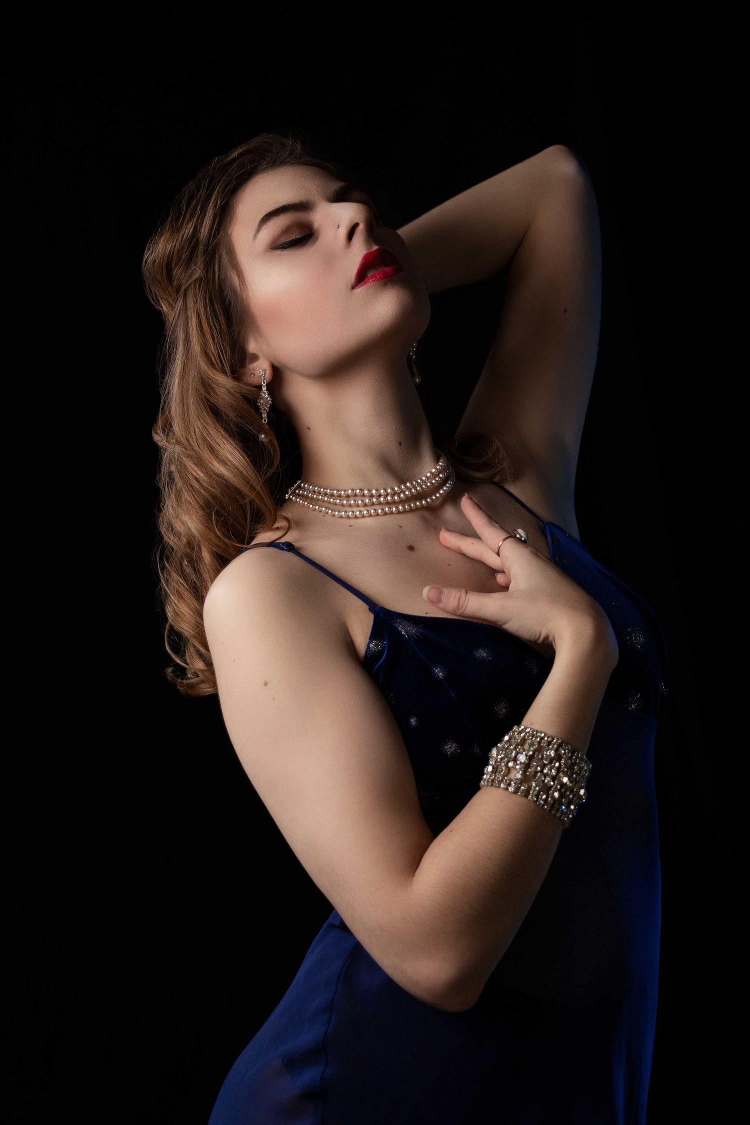 Dramatic boudoir portraits in dark lighting featuring elegant jewelry and navy blue attire.