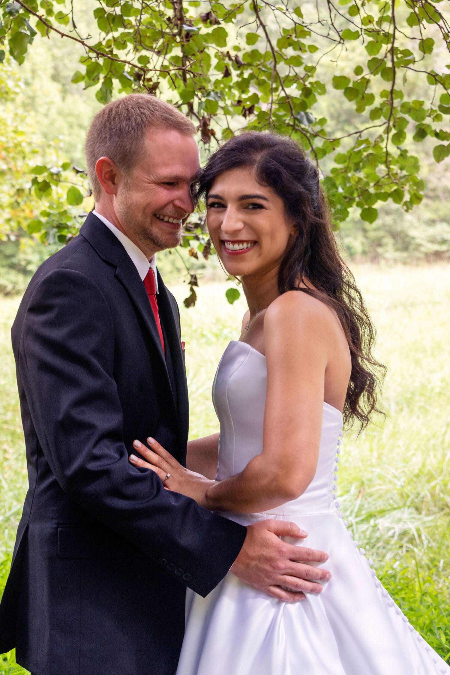 A romantic wedding portrait of a couple embracing under green leaves.