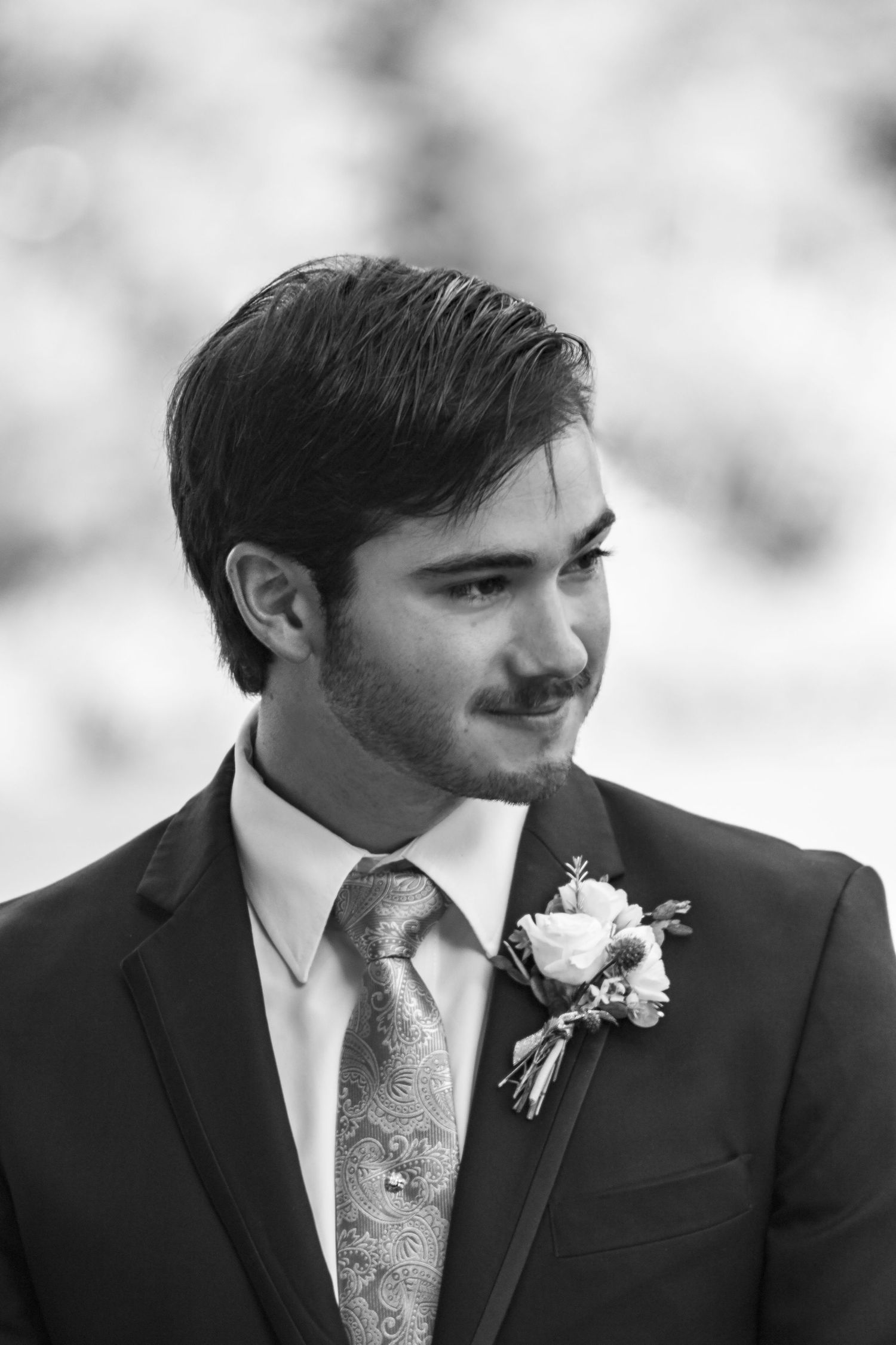 Black and white portrait of a groom wearing a boutonniere and patterned tie.