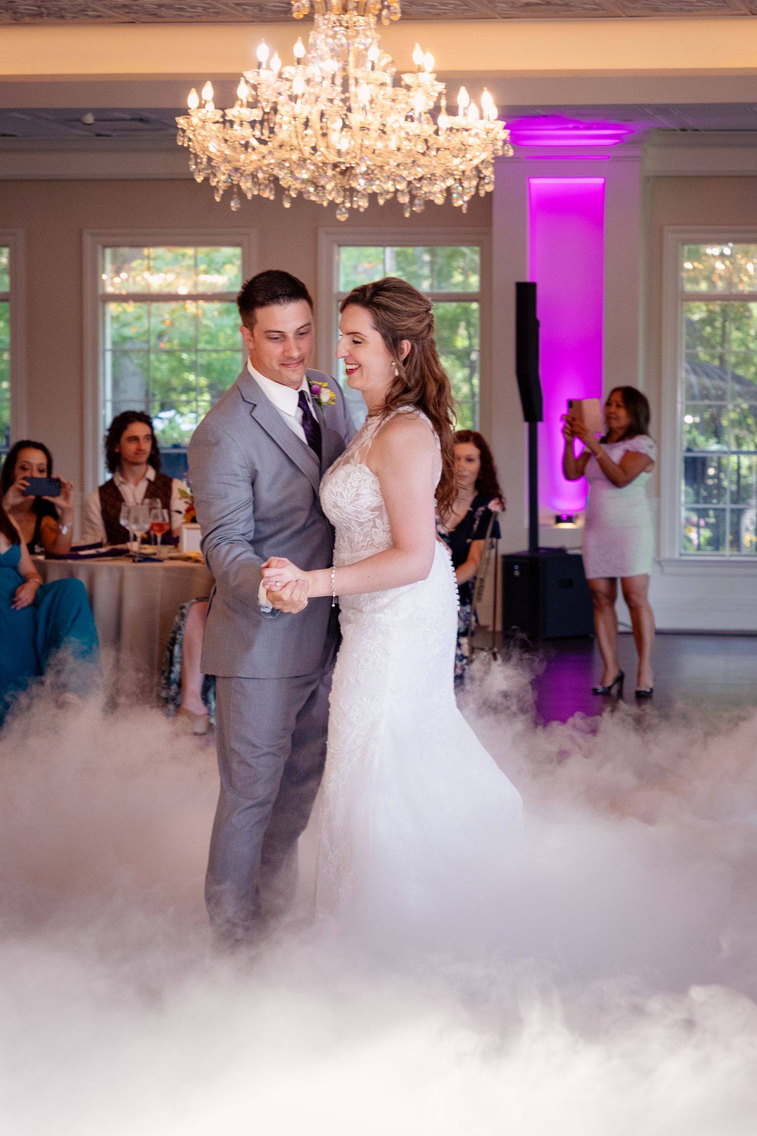 Newlyweds share their first dance surrounded by fog effects and purple lighting.