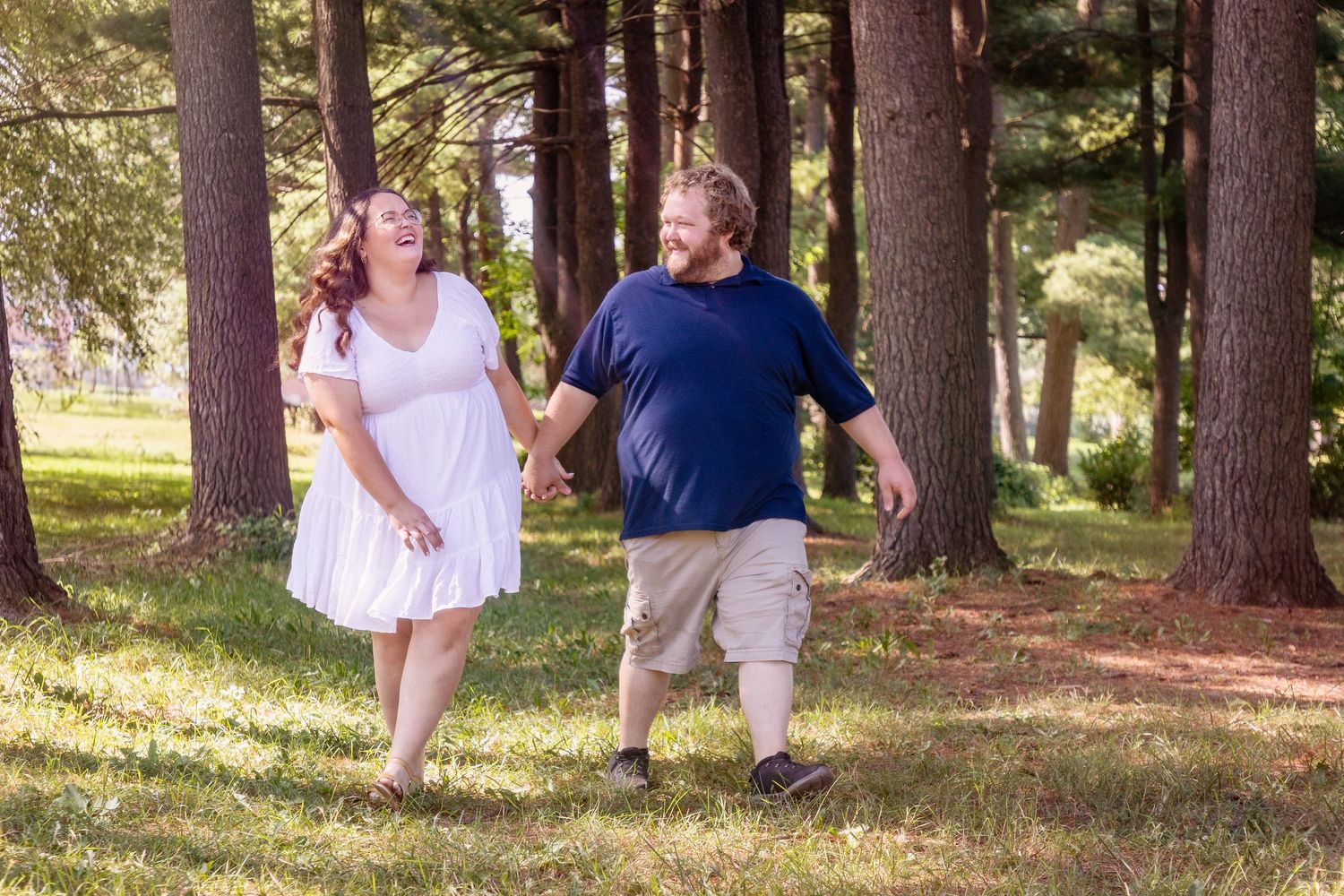 Playful couple enjoys a sunny afternoon among tall pine trees.