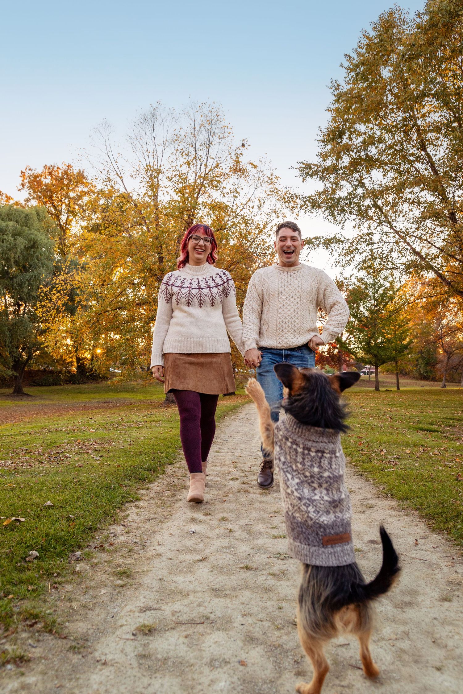 Couple walking with their dog on a dirt path surrounded by autumn trees.