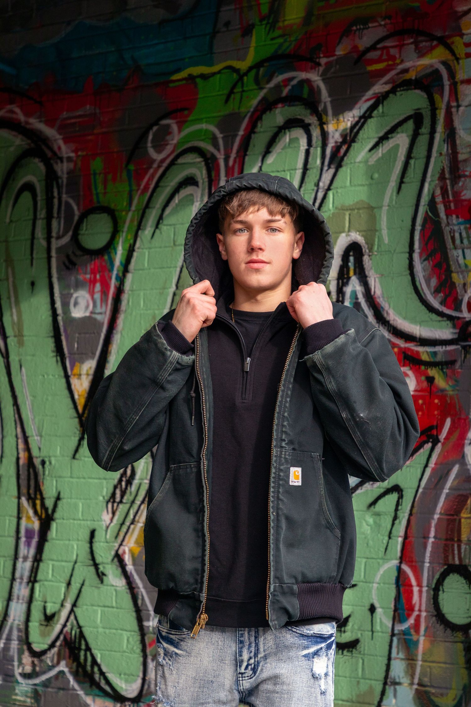 Urban portrait series against colorful graffiti wall featuring casual black jacket and bucket hat styling.