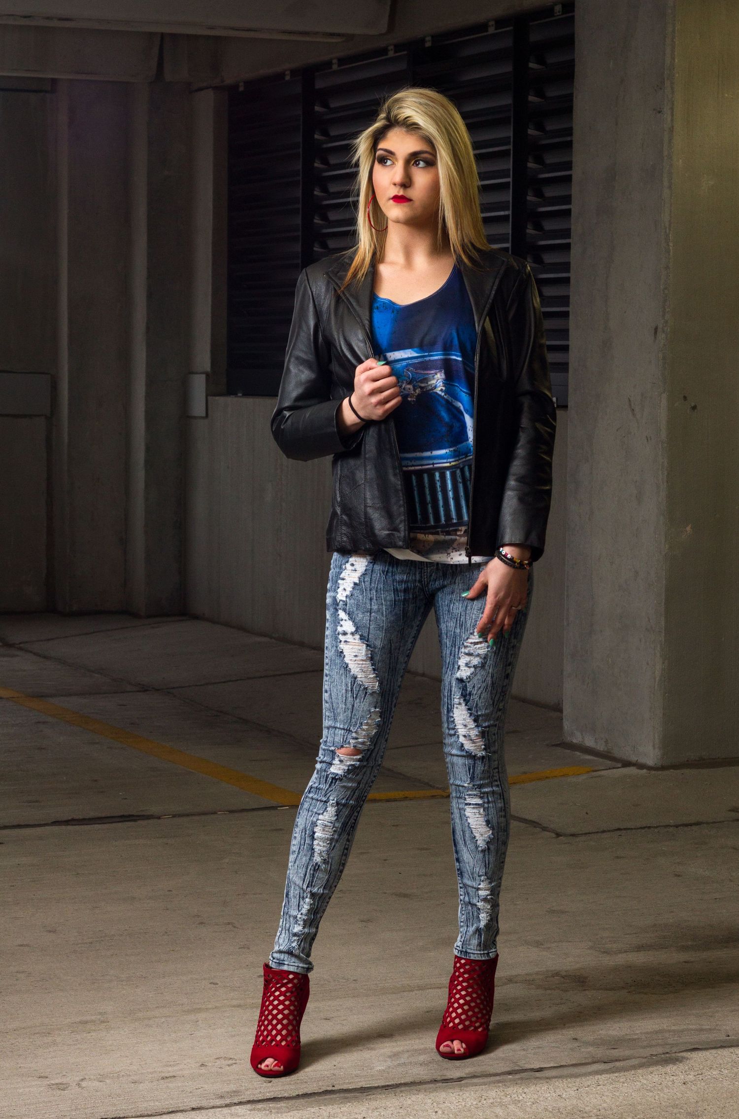 Person wearing distressed jeans and blue top posing in a parking garage.