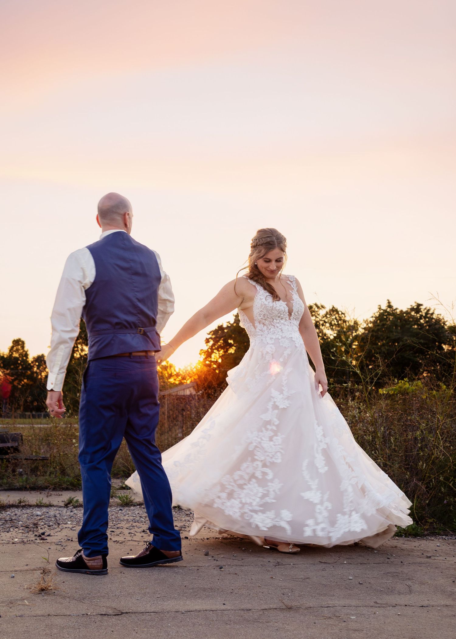 Couple dances playfully at sunset with bride's dress twirling in golden light.