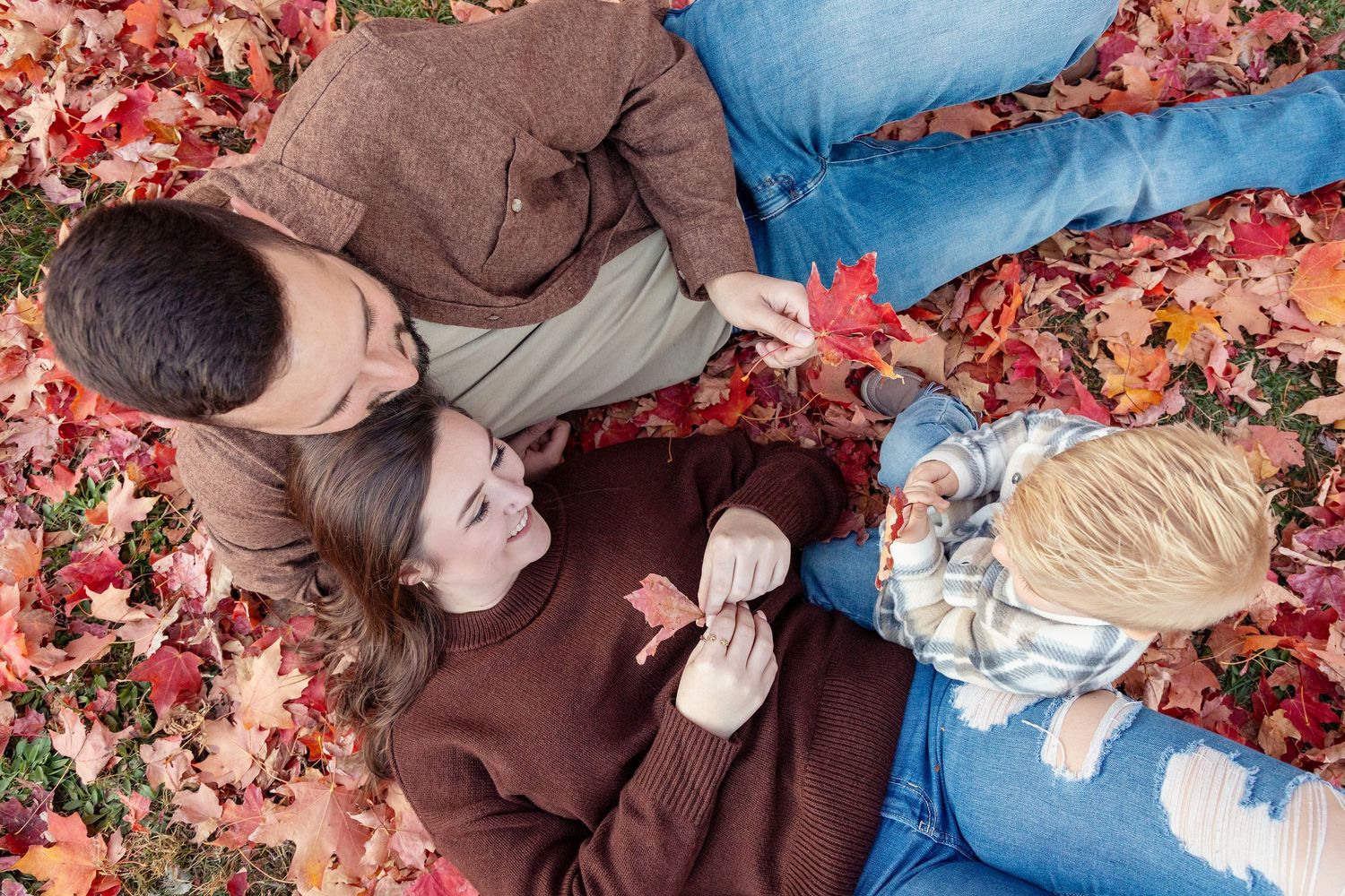 People lying in colorful autumn leaves during fall season photoshoot.