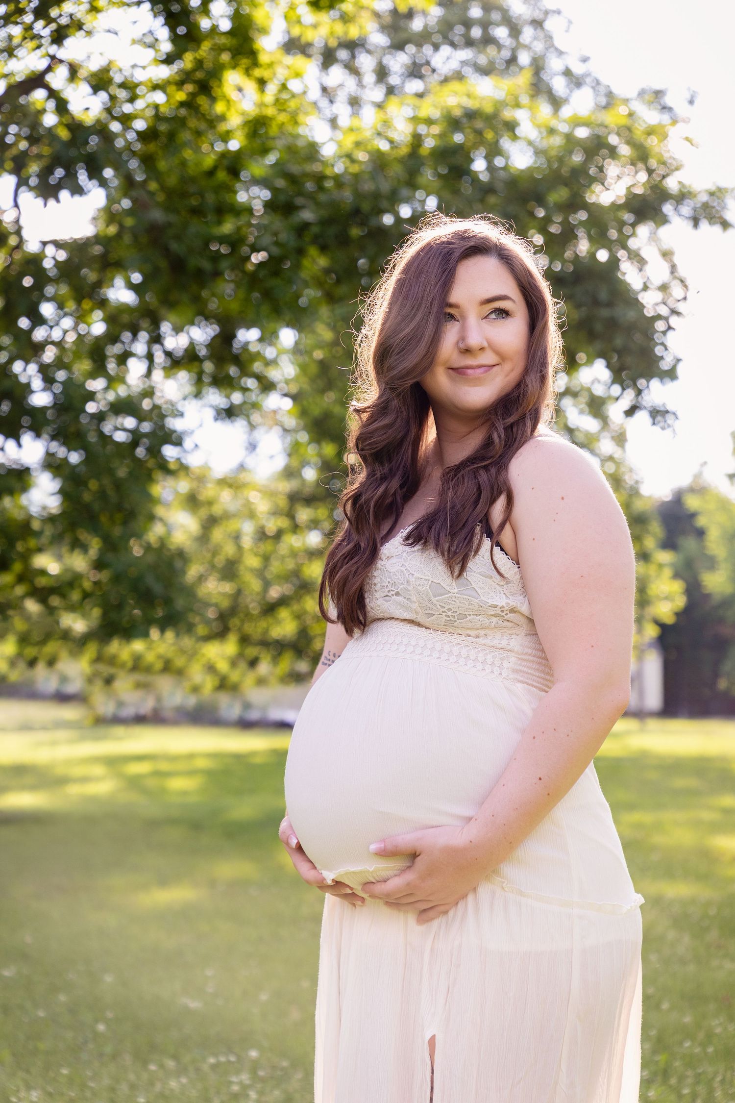 A maternity portrait session in a sunny meadow featuring a white lace dress.