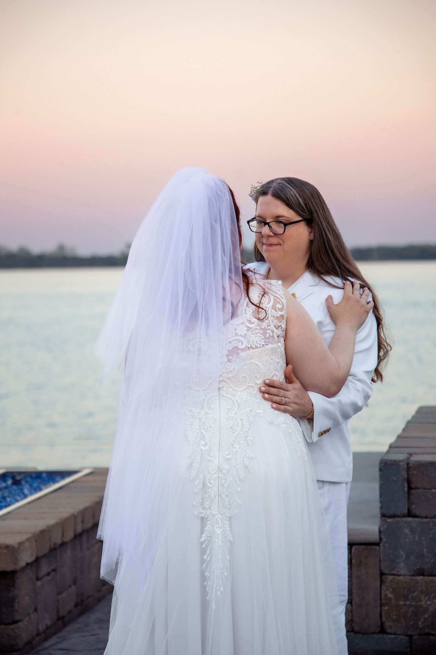 Romantic waterfront wedding photos at sunset with couple in white attire.