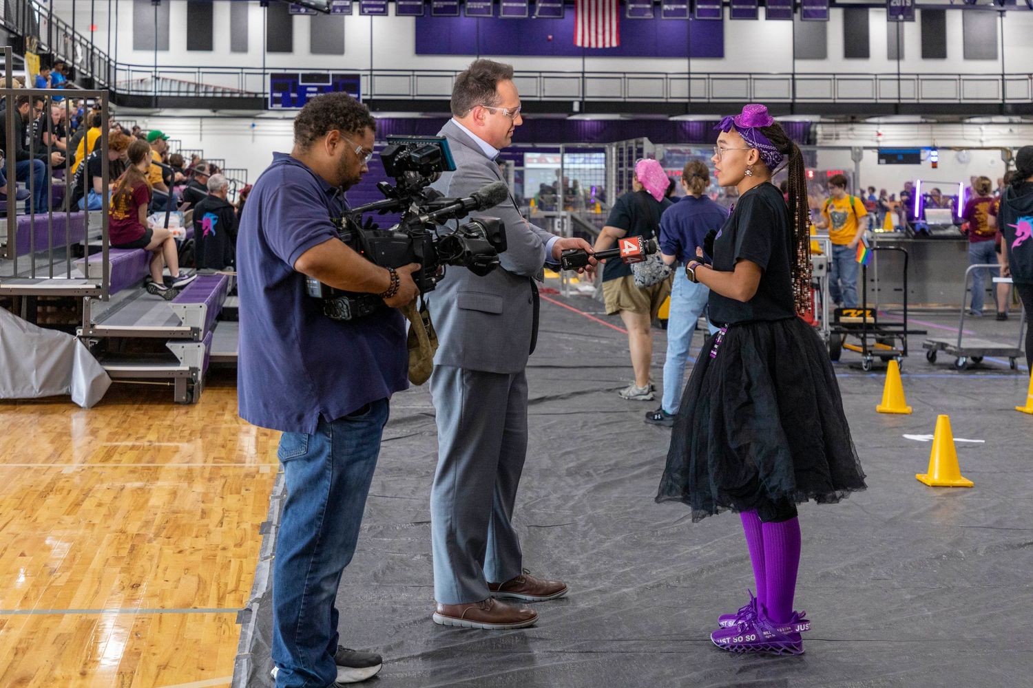 Crowd gathering in a school gymnasium with purple and yellow decor.