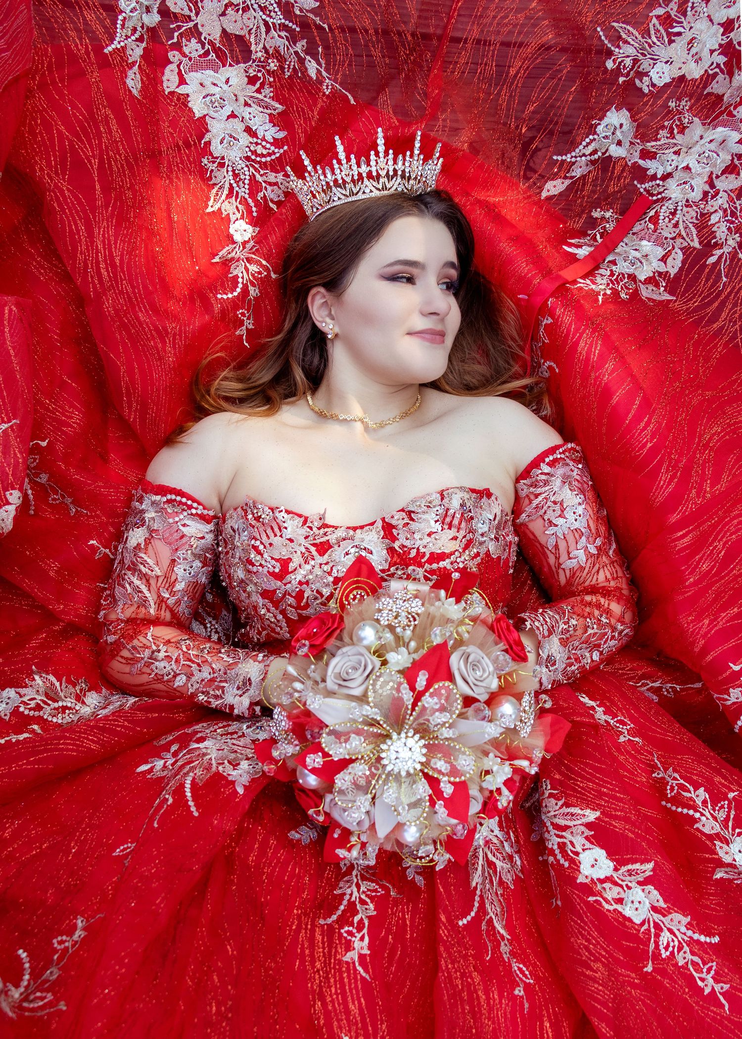 An elegant red and white lace ballgown displayed against a matching red backdrop.