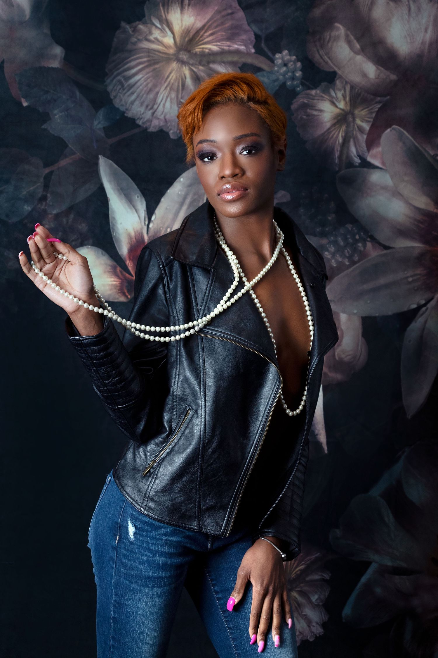 Stylish portrait against a dark floral backdrop with pearl necklace and leather jacket.