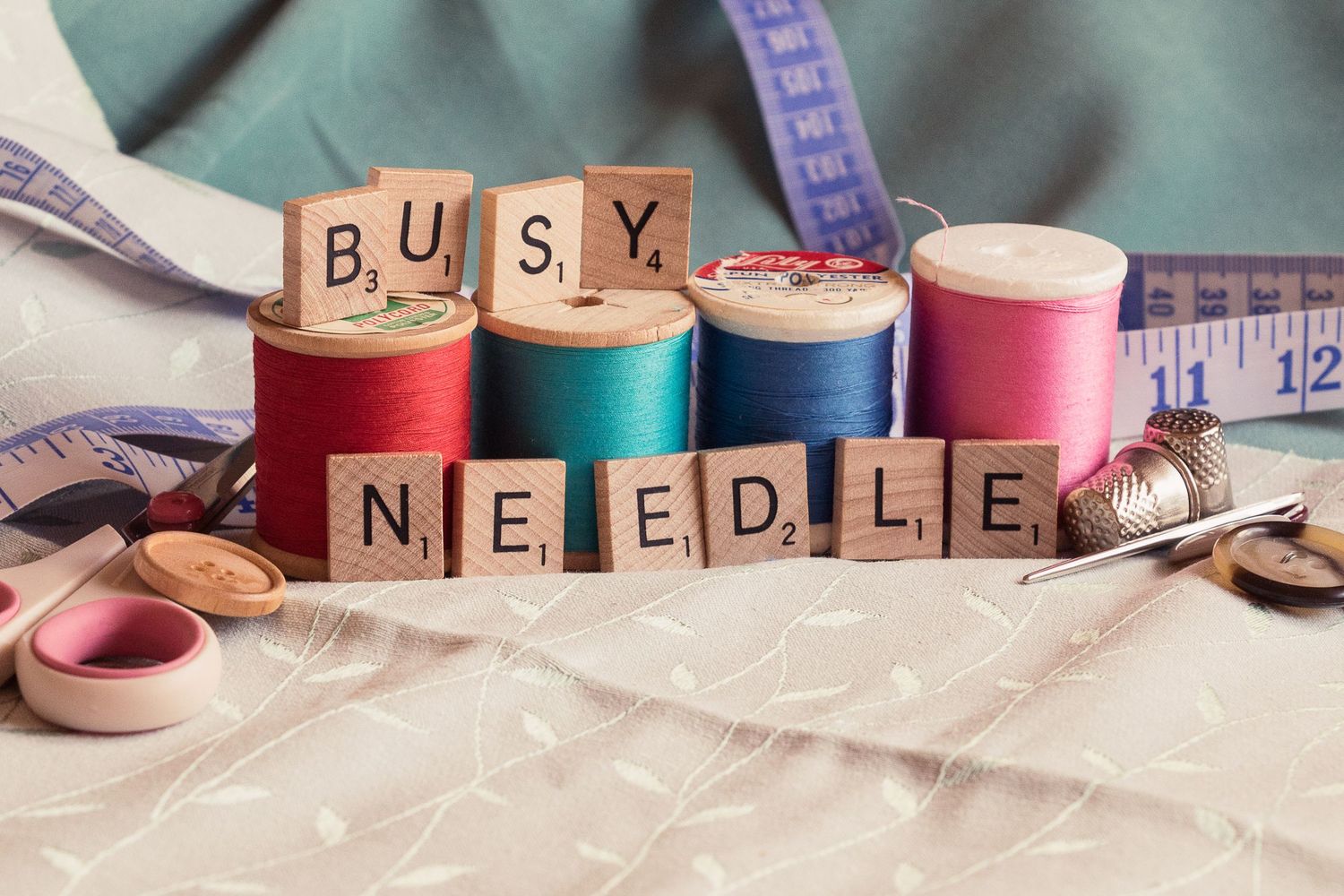 Sewing supplies including colorful thread spools, scissors, and Scrabble letter tiles spelling out 'BUSY'.