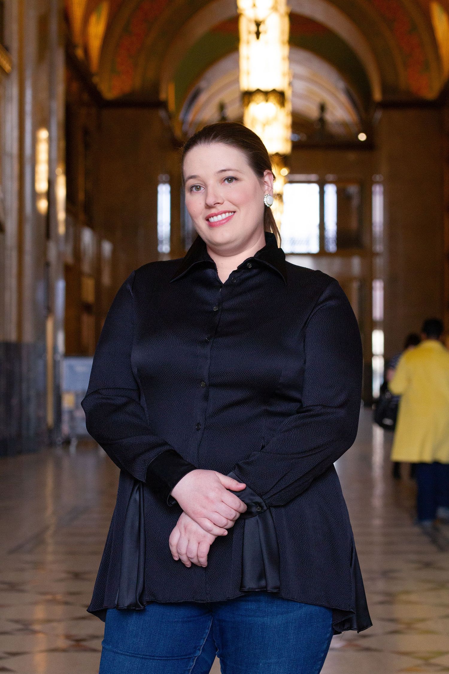 Person in black ruffled blouse posing in ornate architectural setting with arches.