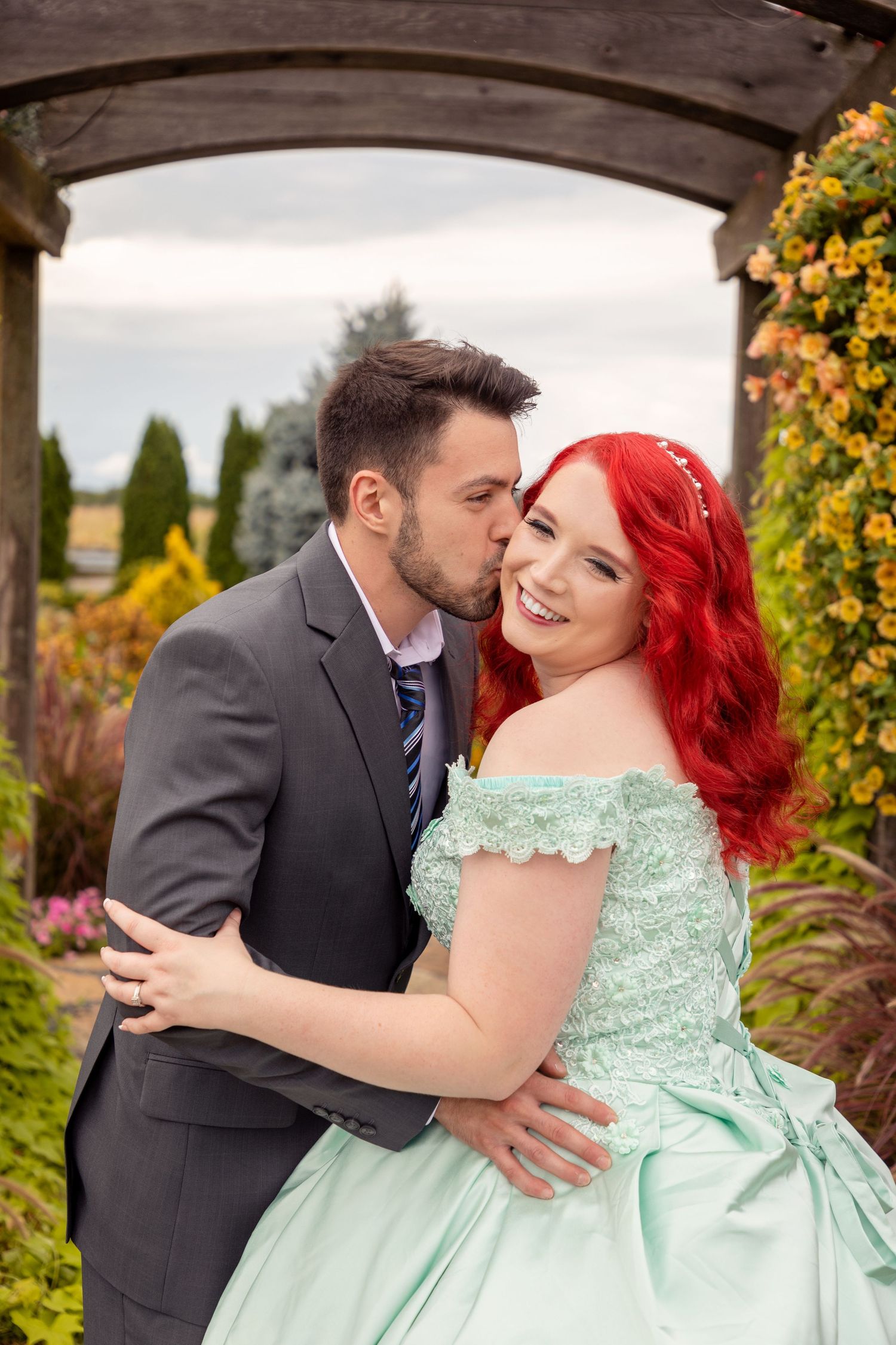 Romantic couple embracing under an archway surrounded by autumn flowers and greenery.
