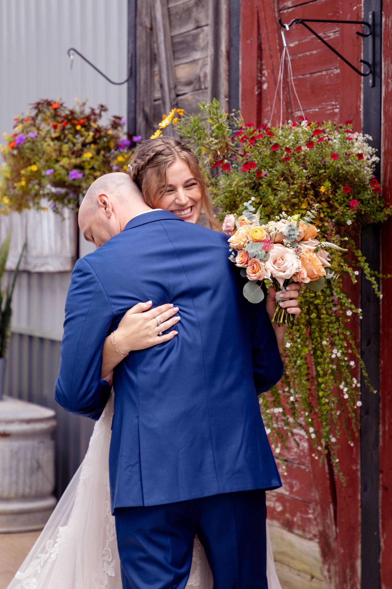 Couple shares intimate moment in front of rustic red barn with hanging flower baskets.