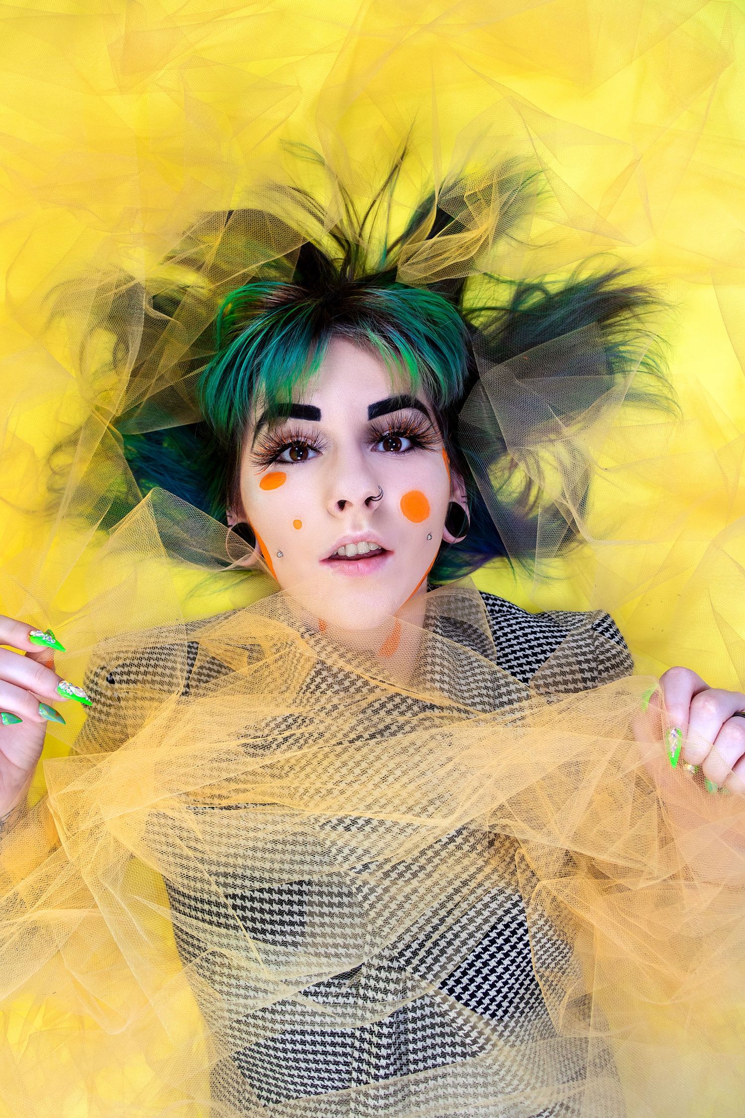 Artistic portrait with yellow tulle and teal hair creating ethereal effect against bright yellow backdrop.