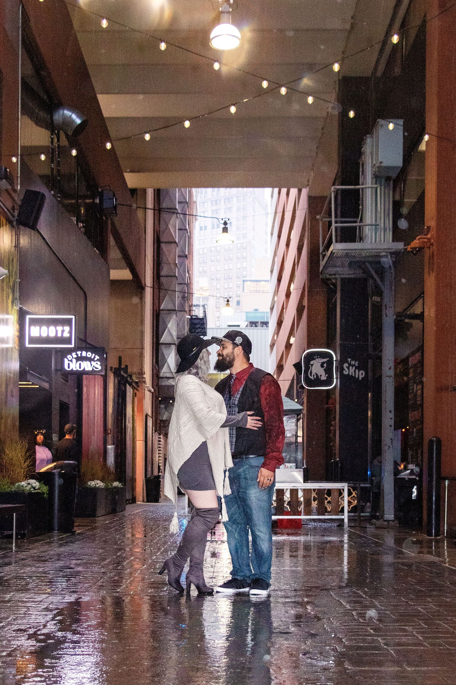 A romantic moment under string lights in a rainy urban alley.