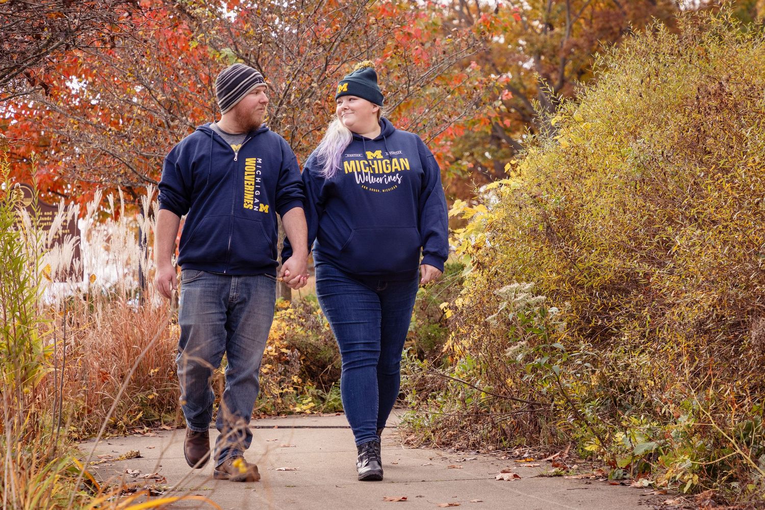 A couple takes a romantic autumn walk wearing matching university sweatshirts.