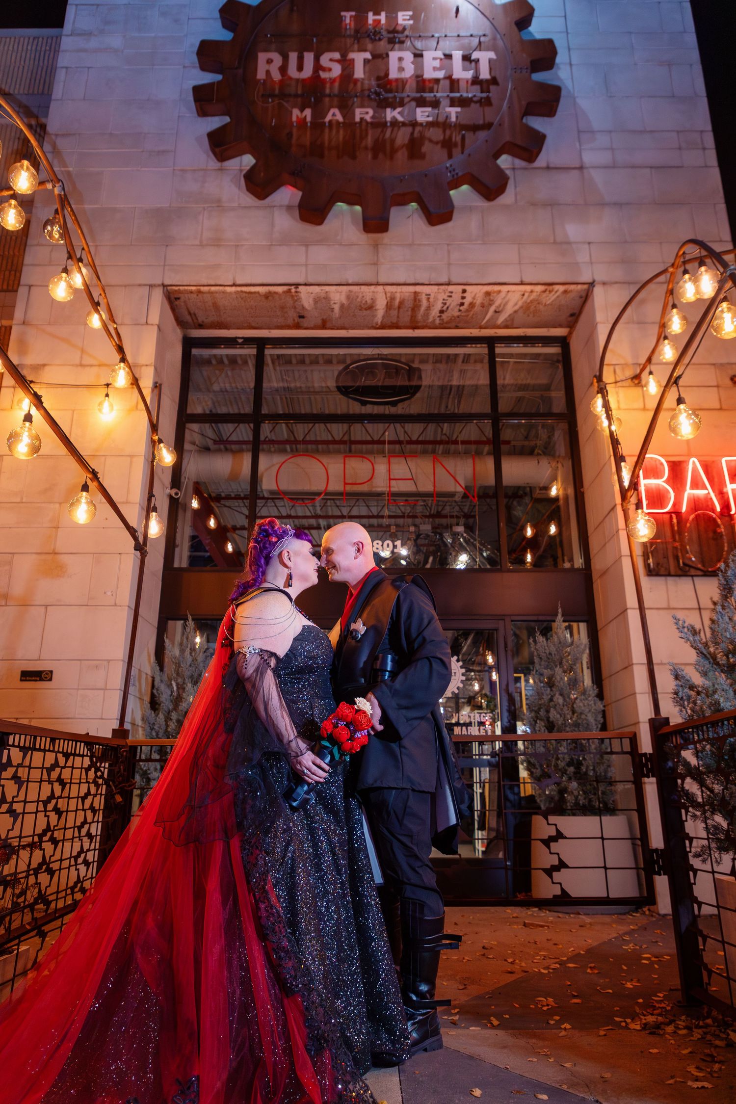 Evening wedding photos outside an industrial venue with string lights and brick walls.