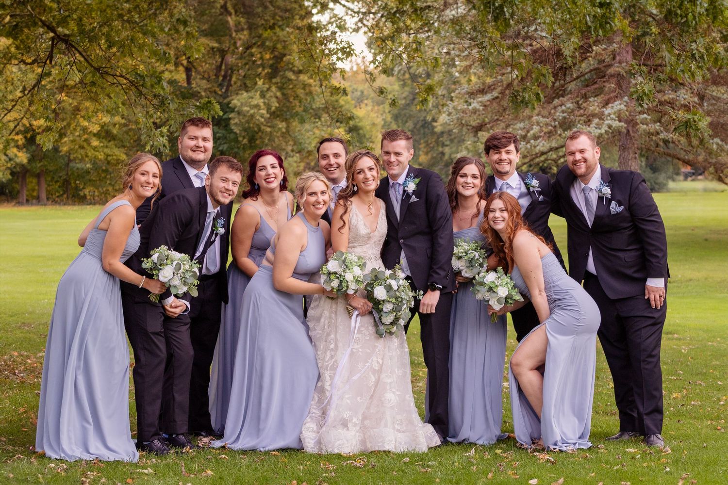 Wedding party in blue bridesmaid dresses and dark suits posing outdoors.