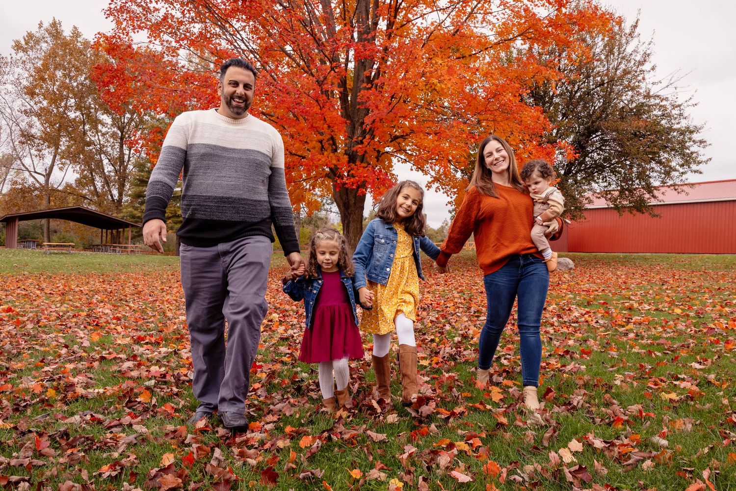 Group playing together in colorful autumn leaves with red barn in background during fall season.
