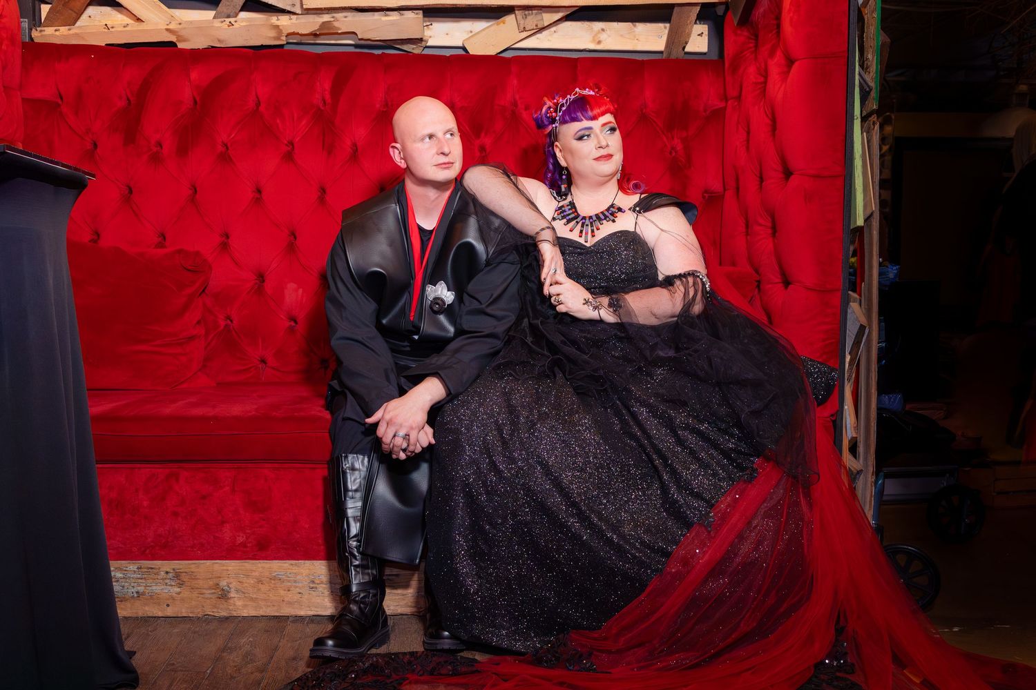 Stylized wedding portraits on red velvet couch with dramatic lighting.
