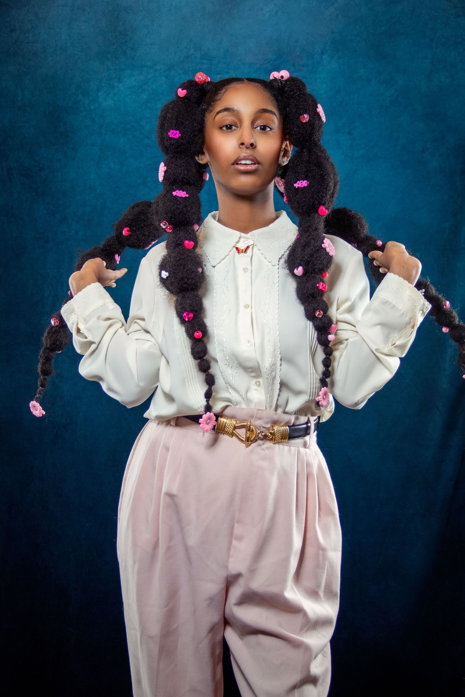 Portrait series showing playful poses in white outfit with floral-decorated hairstyle against blue backdrop.