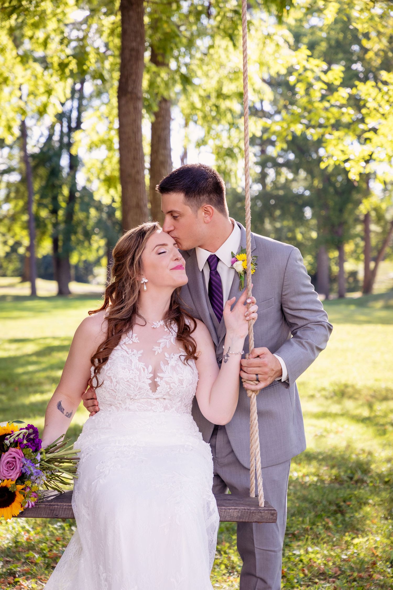 Romantic wedding couple sharing an intimate moment on a swing in a sunlit garden with autumn foliage.