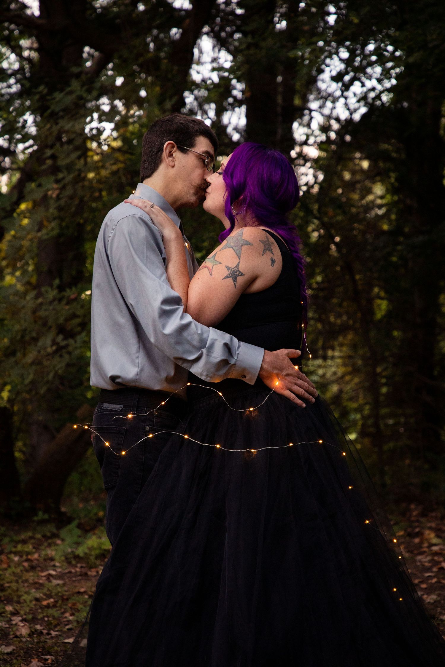 A romantic moment captured in the woods with string lights and formal wear.