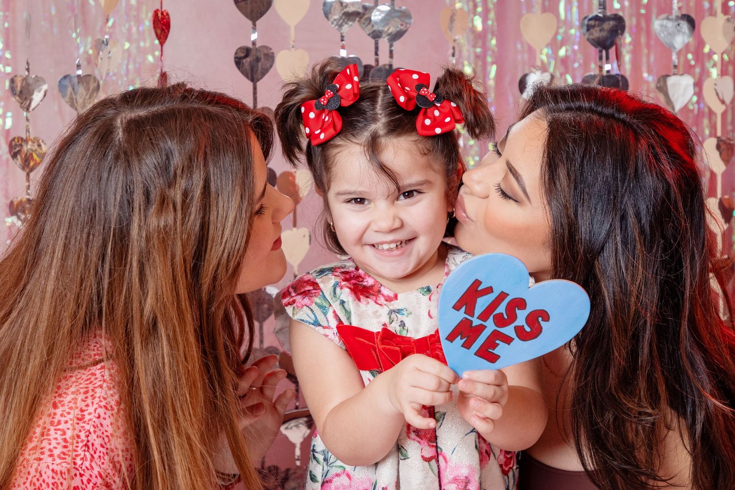 Valentine's themed photoshoot with pink backdrop, silver streamers, and heart decorations.