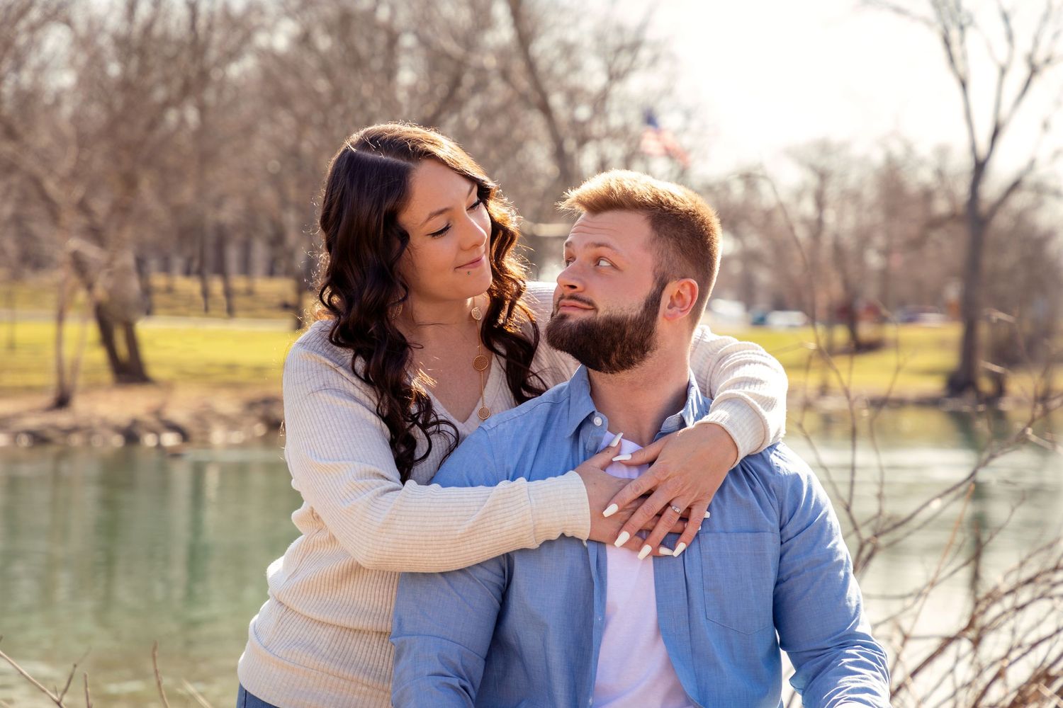 A couple shares a tender moment by a lake during winter, wearing casual attire.