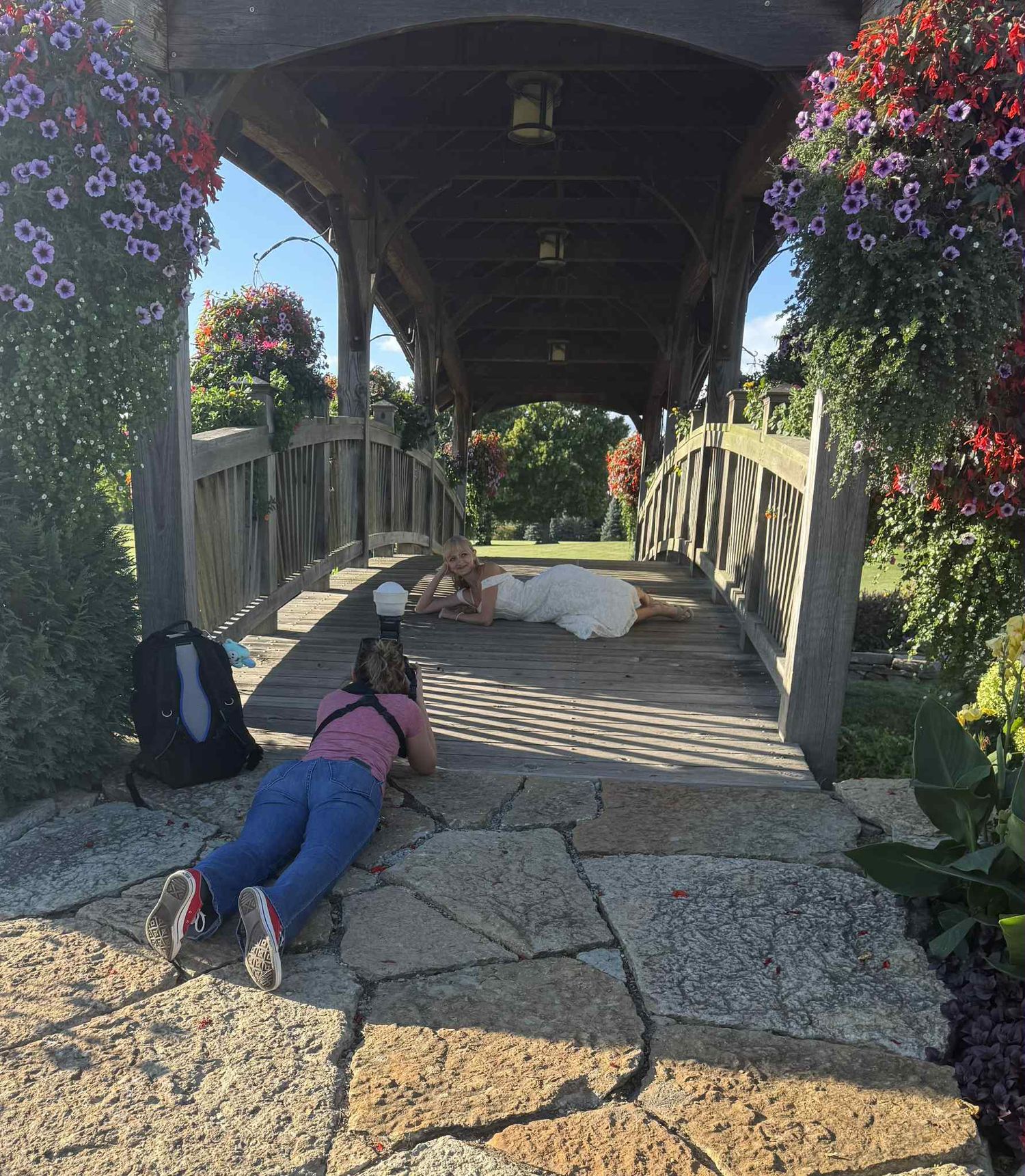 Person lying on stone pathway surrounded by hanging flowers and greenery.