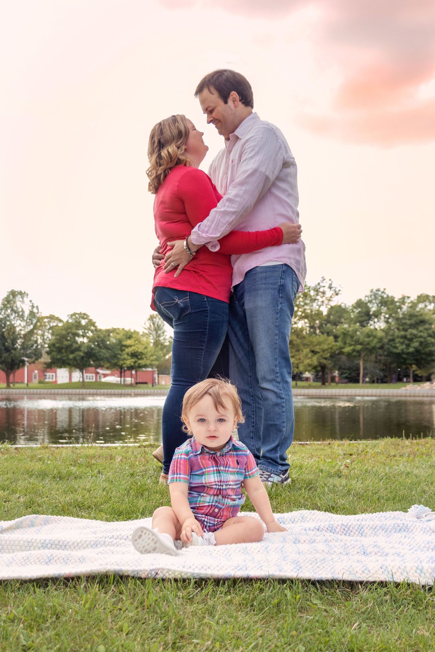 Family having a picnic on a blanket in a grassy field with a red barn in the background.