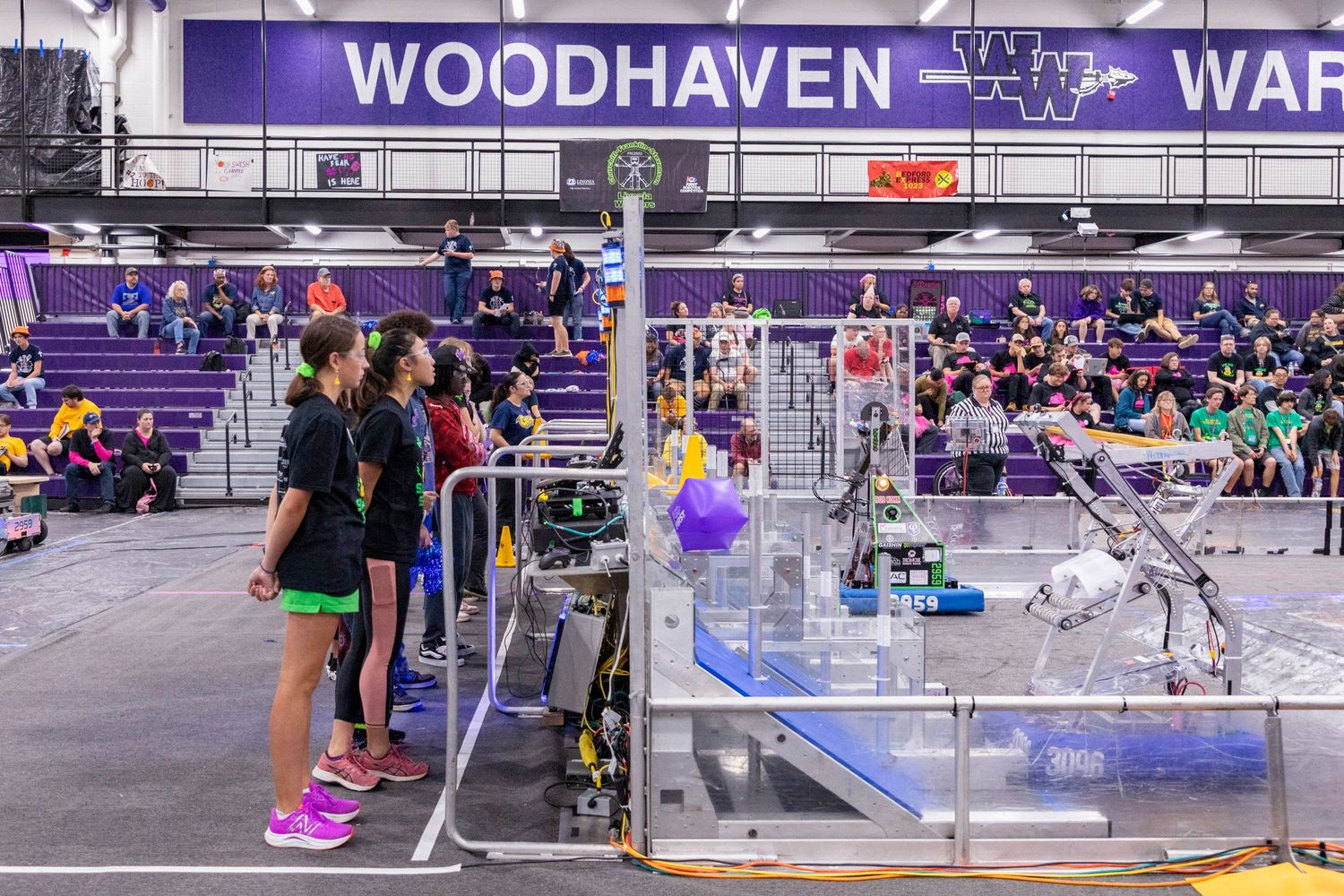 Wide view of a school gymnasium with purple seating and Woodhaven Warriors signage.