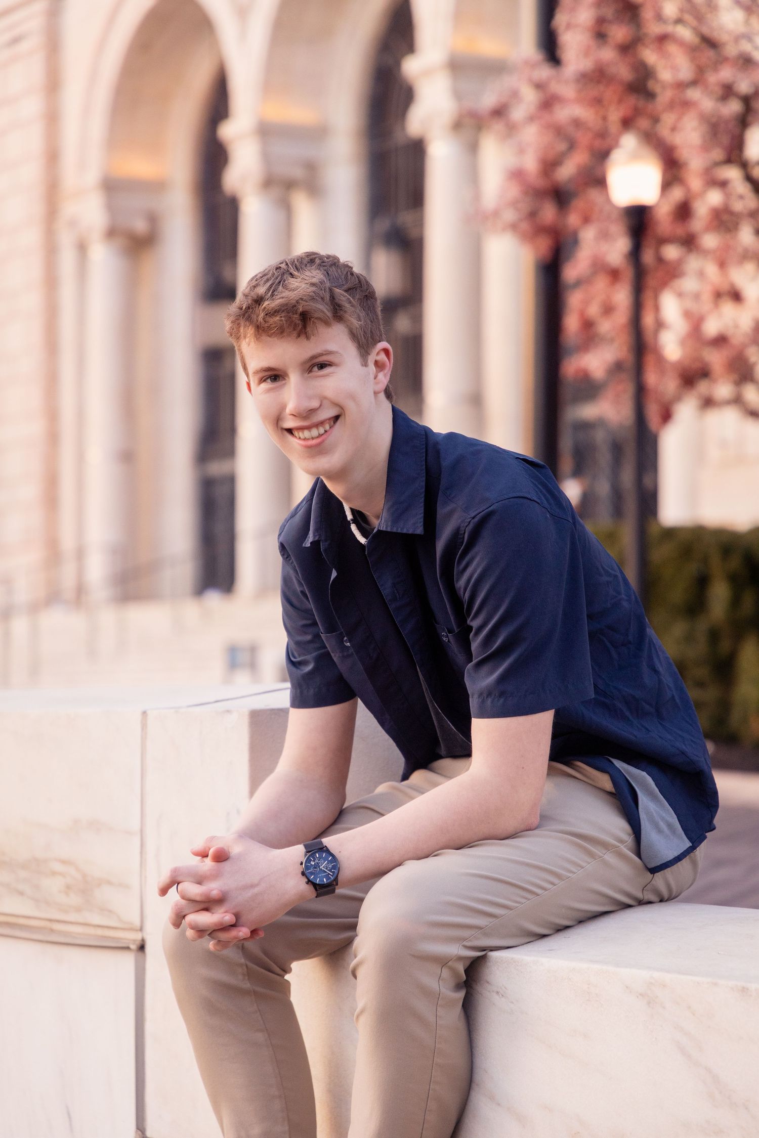 A casual portrait of someone sitting outdoors on stone steps near classical architecture.