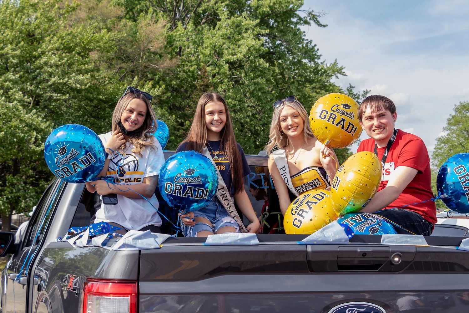 Group poses with colorful pool floats in the back of a Ford pickup truck on a sunny day.