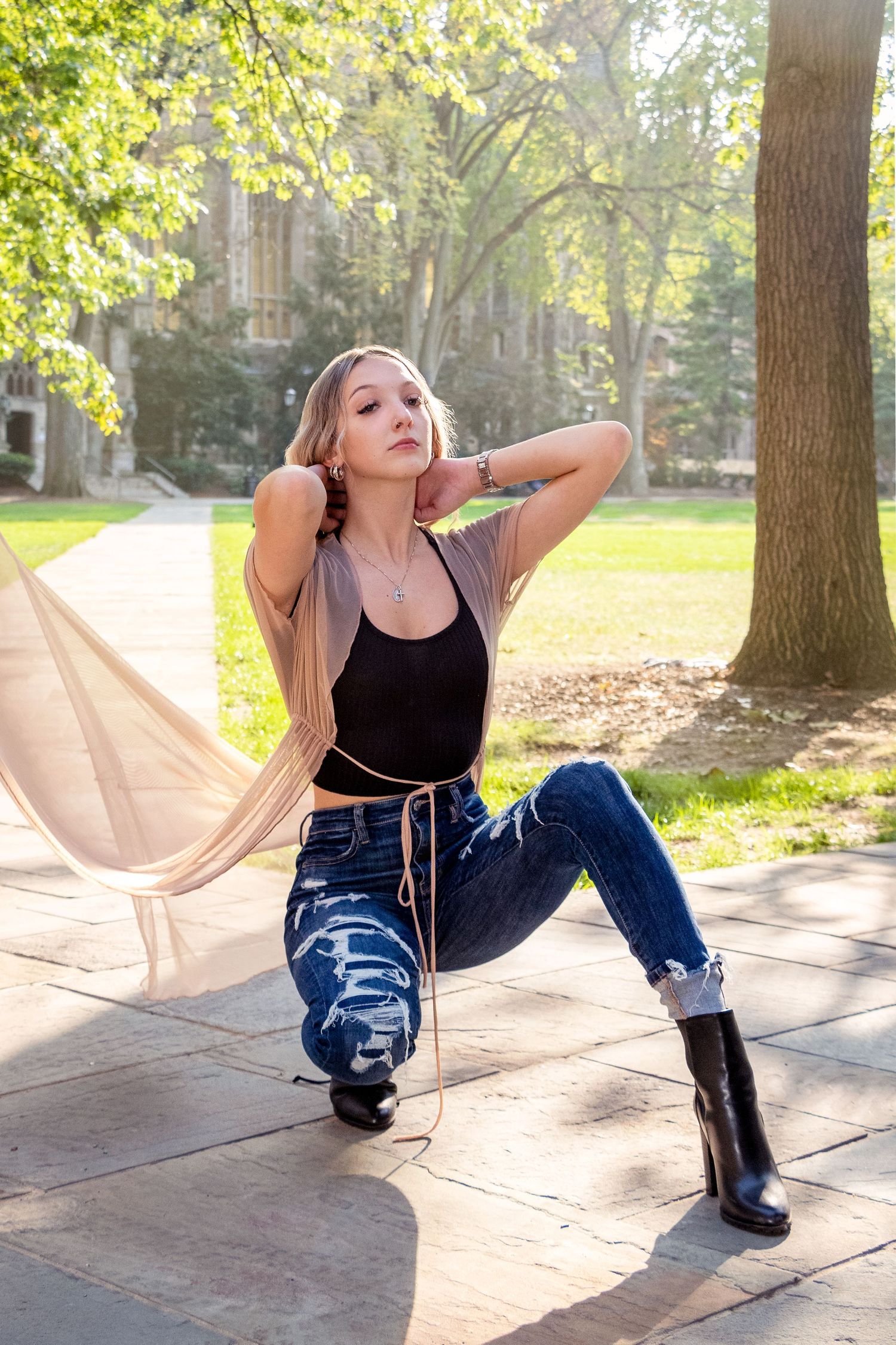 Stylish portrait of someone posing on stone steps with flowing fabric in a sunny campus setting.