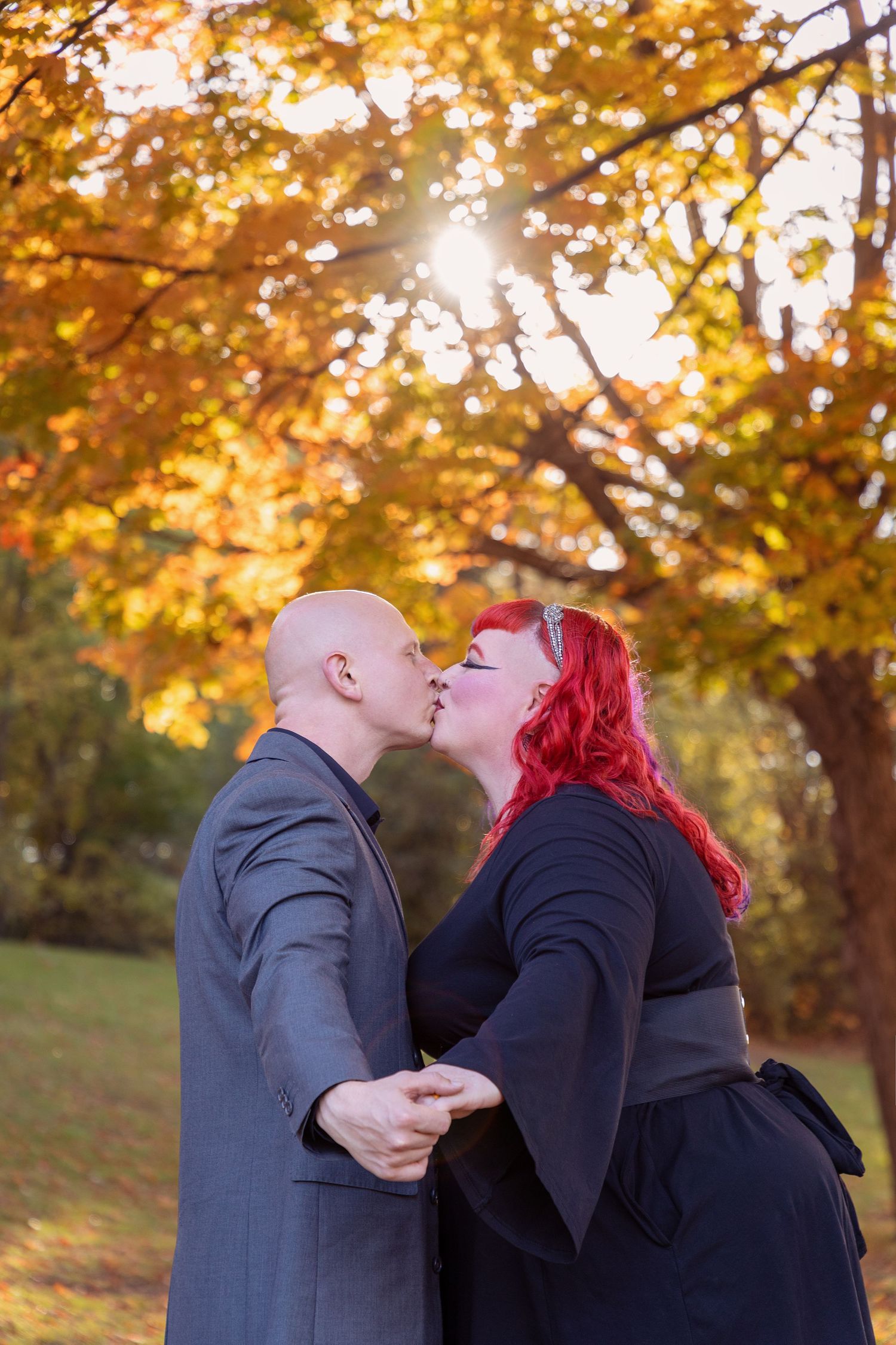 Romantic couple sharing a kiss against a backdrop of golden autumn leaves at sunset.