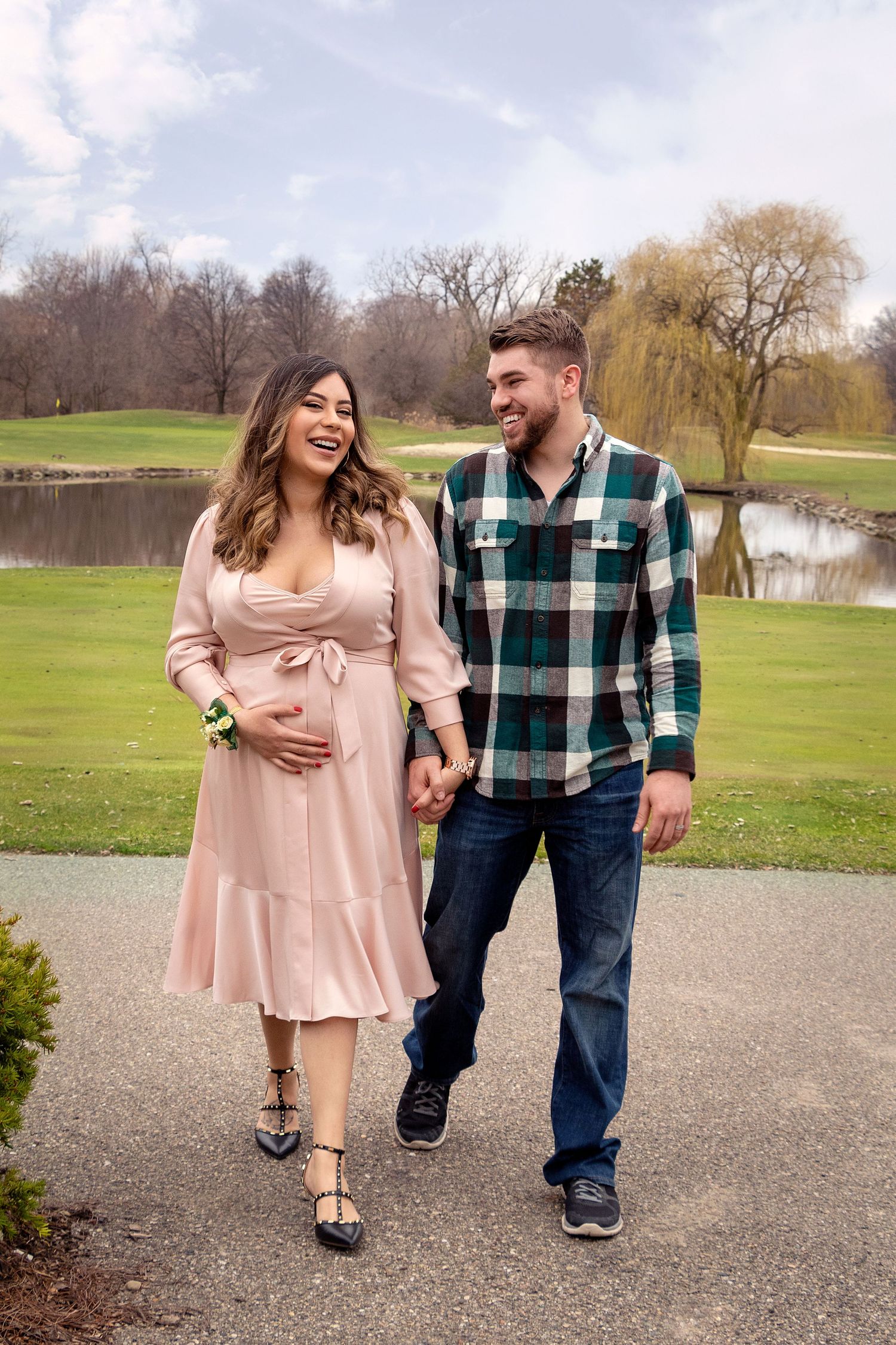 Happy couple walking and laughing together on a path with scenic lake and trees in background.