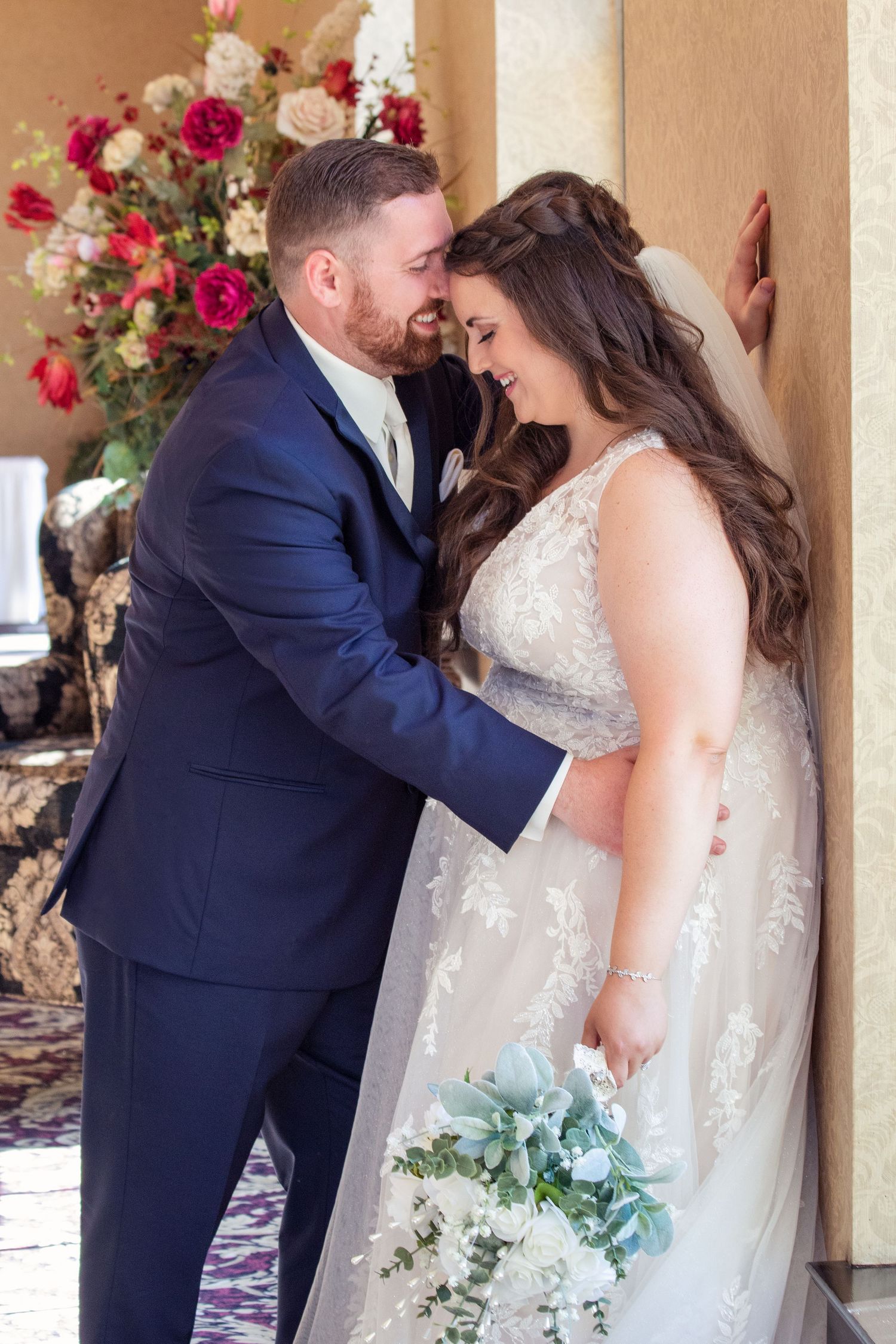 Indoor wedding portraits with couple against floral backdrop in warm lighting.